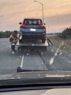 Black SUV on a flatbed tow truck, rainy day