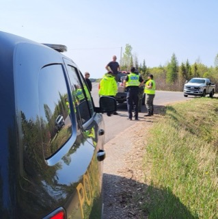 Police officers and paramedics attend to an injured person near two pickup trucks on a rural road.