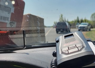 Redline radar detector on a dashboard, vehicles on highway in background