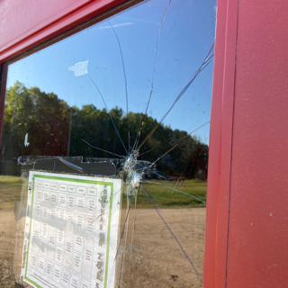 Broken window with a sign visible through it, grassy field and trees in background