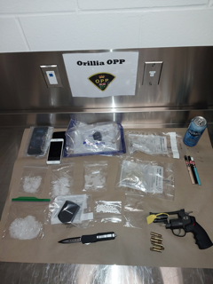 Orillia OPP logo. White powder, pills, a smartphone, a knife, a handgun, and various small bags on a metal surface.