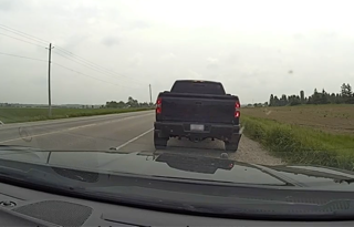 Black pickup truck on a wet road, green field and trees in background