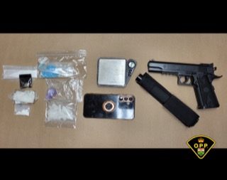 Several small baggies of a white and blue substance, a black smartphone, and a black handgun on a tan surface.