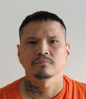 Man with short dark hair and mustache, visible tattoos on neck, orange shirt