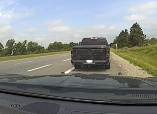 Black pickup truck ahead on a two-lane road, green trees and sky in background