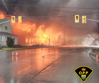 Orange flames and smoke fill the sky behind a wet street.