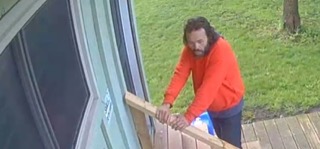 Man in orange sweatshirt and jeans, holding a wooden plank.