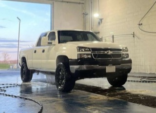 White pickup truck with black wheels, standing in a car wash