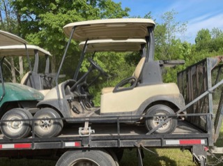 Two beige golf carts on a trailer.