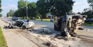 Two cars involved in a collision, one overturned, debris on the road
