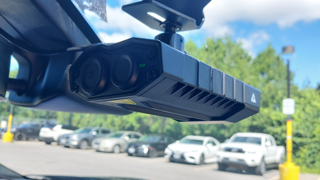 Dashcam mounted on a windshield, cars in a parking lot, green foliage, blue sky