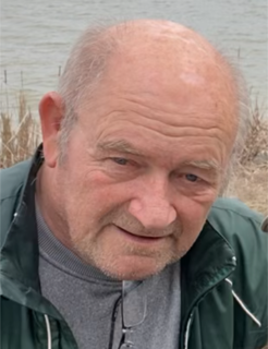 Older man with a slight smile, green jacket, gray sweater