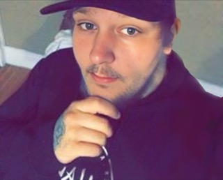 Man wearing a black baseball cap and hoodie, looking at the camera