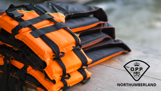 Orange and black backpacks stacked on a gray surface. Northumberland logo.