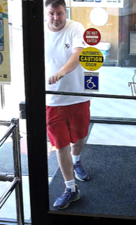 Man in a white t-shirt and red shorts walking towards a door.