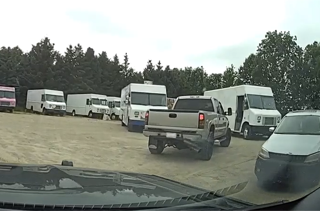 Several white vans and a pickup truck parked on gravel.