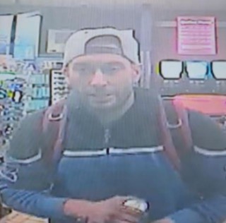 Man wearing a black baseball cap and jacket, holding a cup