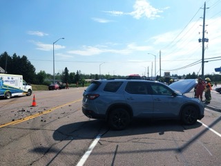 Damaged gray SUV, ambulance, and police vehicles on a road.