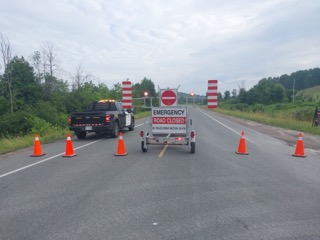 Police truck blocking a road, orange traffic cones, road closed sign