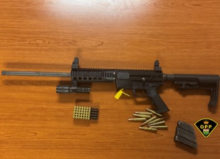 Black AR-15 style rifle, magazines, and ammunition on a wooden surface.