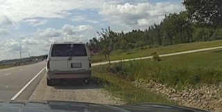 Van parked on the shoulder of a highway, grassy hill behind it, cloudy sky