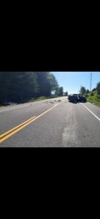 Debris on a two-lane road, damaged vehicles visible in the distance
