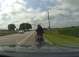 Person on a red motorcycle, wearing a white helmet and black jacket, traveling on a paved road.