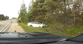 Damaged white car off the shoulder of a highway, trees and foliage in background