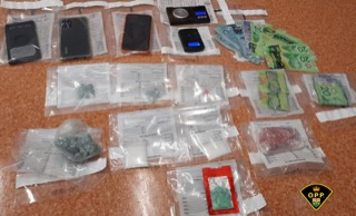 Small baggies of green substance, Canadian twenty-dollar bills, scales, and evidence tags on a red surface.