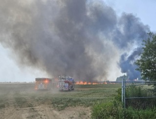 Firefighters and a fire truck on a field, large smoke cloud in the background
