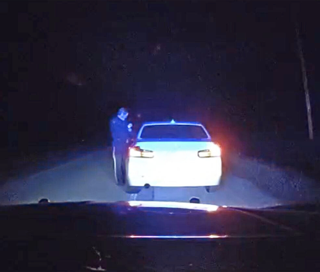 Police officer standing next to a police car with flashing blue lights.