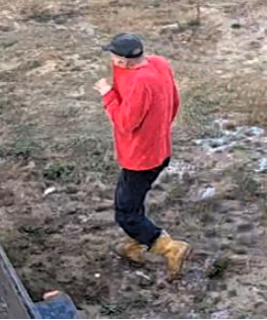 Person wearing a red sweatshirt and black pants walking on dirt.