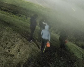Person walking uphill in fog, carrying an orange bucket