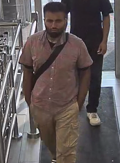 Man in a short-sleeved shirt and khaki pants, carrying a black strap across his chest.