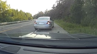 Silver sedan on the shoulder of a highway, green foliage in background