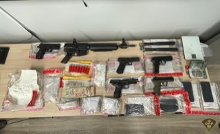 Firearms, ammunition, cash, and drug paraphernalia on a white surface.