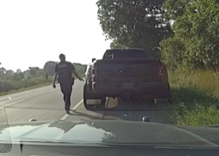 Person in dark clothing walking toward a lifted black pickup truck on a roadside.