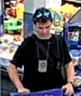 Person wearing a black t-shirt and black hat, standing behind a DJ setup.