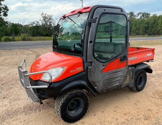 Red Kubota utility vehicle with a front snow plow attachment.