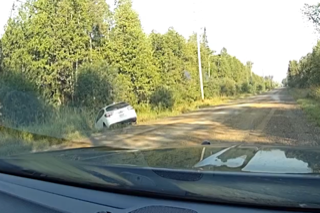 White SUV driving on a dirt road, surrounded by green trees