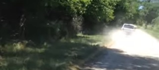 Vehicle driving on a dirt road, dust cloud visible