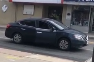 Black Nissan Altima driving down a street