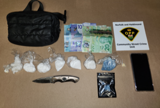 Several baggies of white powder, Canadian twenty and ten dollar bills, a black bag, a folding knife, and a smartphone on a surface.