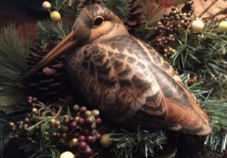 Brown and black bird with a long beak, surrounded by green foliage and berries.