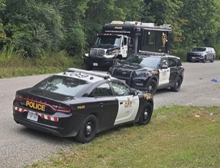 Two police cruisers and a command vehicle parked on gravel.