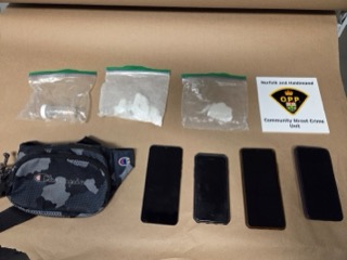 Five baggies of a green substance, a Champion brand fanny pack, and five smartphones on a cardboard surface. Norfolk and Haldimand OPP Community Street Crime Unit