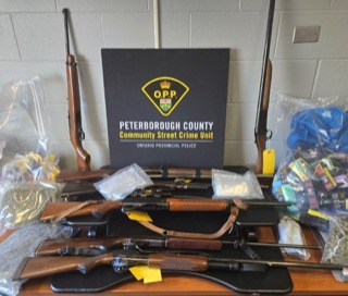 Peterborough County Community Street Crime Unit, O.P.P. Ontario Provincial Police. Several rifles and handguns displayed on a table. Numerous baggies of suspected drugs.