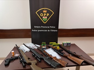 Firearms and ammunition on a table, Ontario Provincial Police logo in background