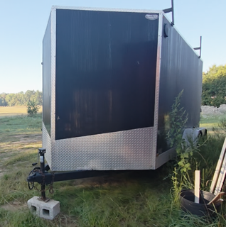 Black utility trailer with diamond plate lower panel, grassy field in background