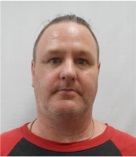 Man with short reddish-brown hair and a silver chain around his neck, wearing a red and black shirt